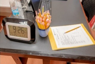 The proctor’s desk in the testing lab with clock, pencils, test record and other items.